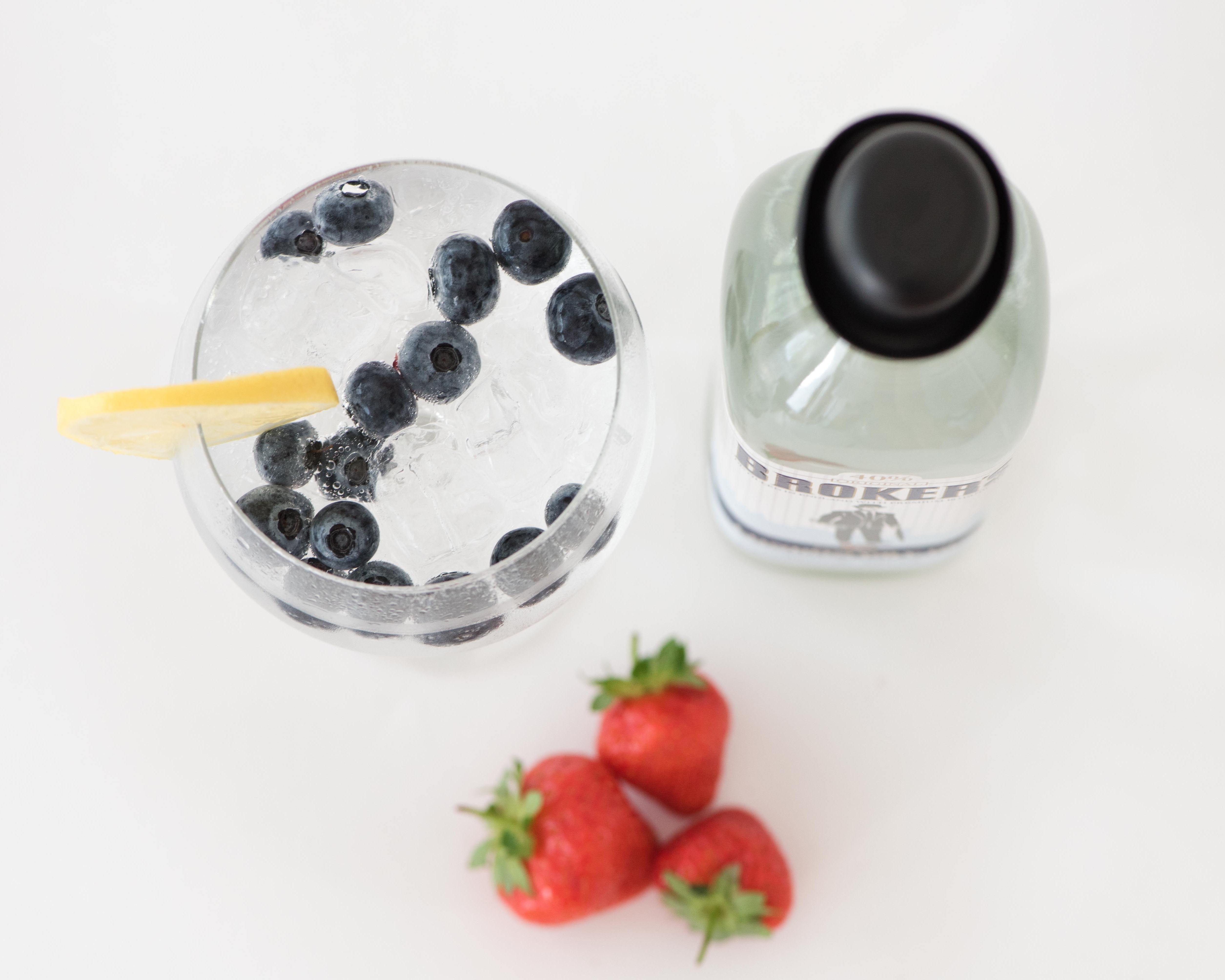 Ein Getränk mit Blaubeeren, Eis und Zitronenscheibe neben einer Flasche und drei Erdbeeren.