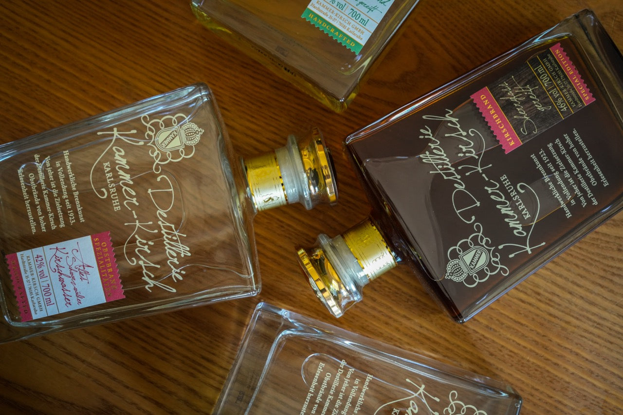 Vier hochkant liegende Flaschen Obstbrand mit goldener Schrift auf einem Holztisch.