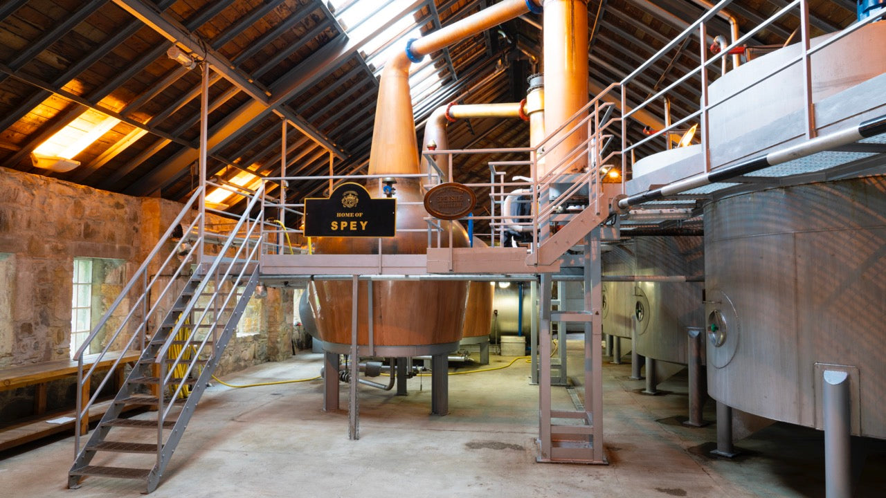 Eine Destillerie mit kupfernen Brennblasen, Metallplattformen und Treppen in einem rustikalen Gebäude.