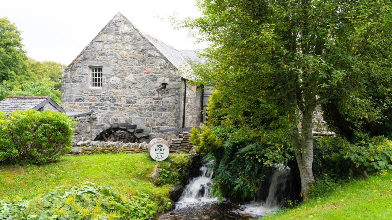 Alte Steinmühle mit Wasserrad und grünem Garten an einem kleinen Wasserfall.