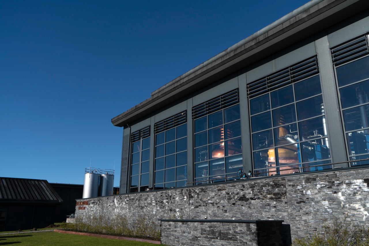Industrielles Gebäude mit großen Fenstern und Kupferbehältern, außen Ziegelsteinmauer, klarer blauer Himmel.