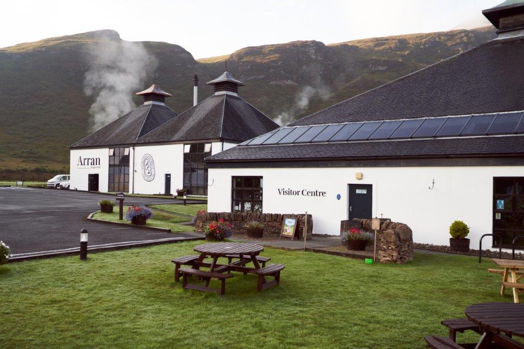 Gebäude einer Brennerei mit Besucherzentrum und Garten, umgeben von grünen Hügeln.