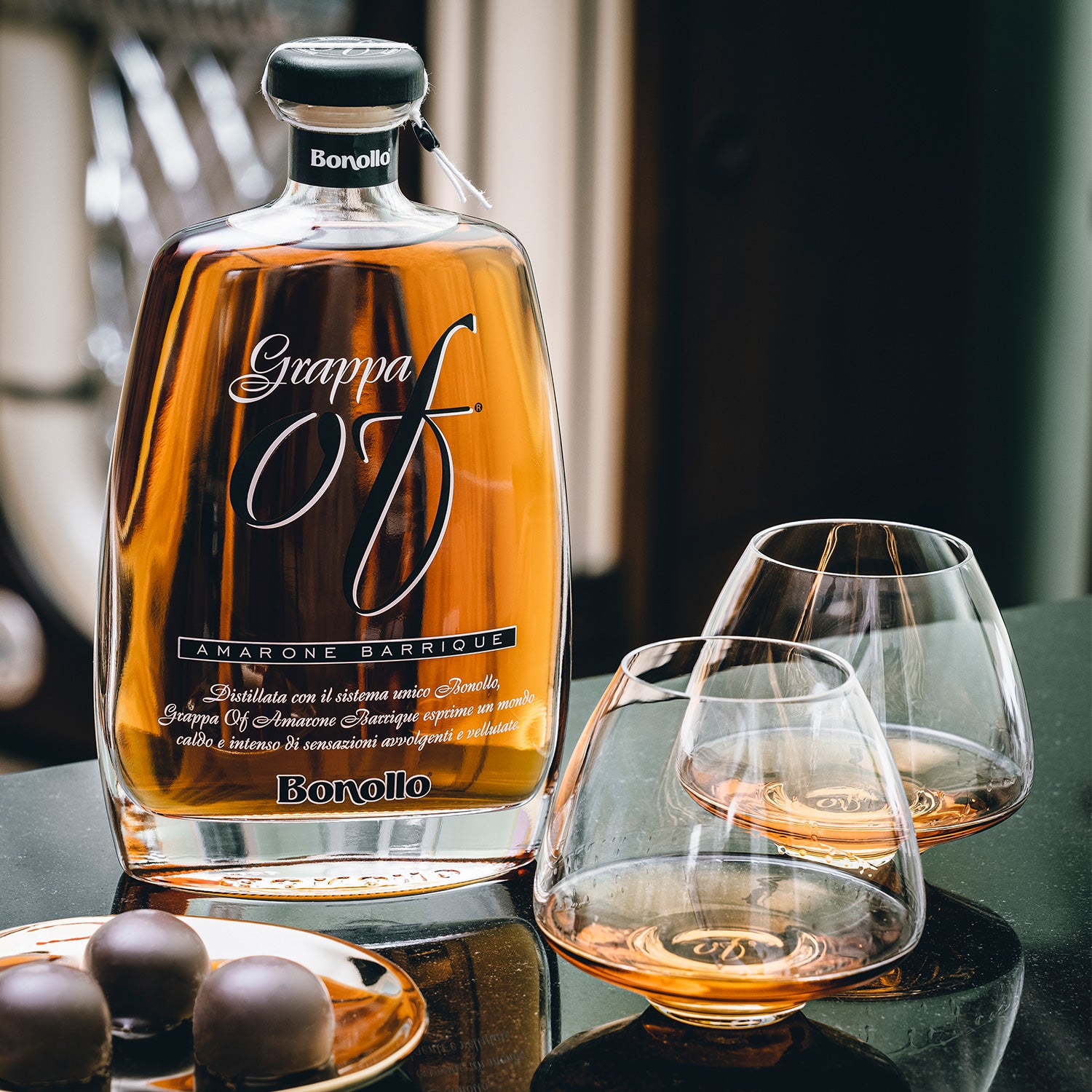 Eine Flasche Grappa mit zwei Gläsern und Pralinen auf einem Tisch abgebildet.