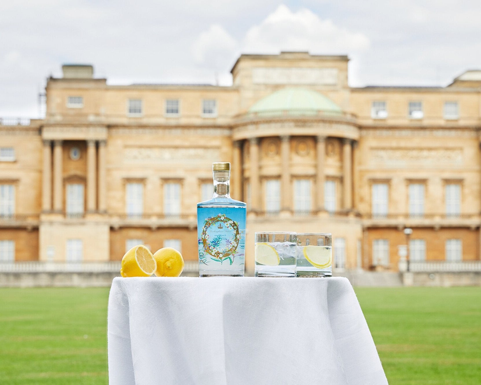 Flasche und Glas Gin mit Zitronen auf Tisch vor einem großen, historischen Gebäude.