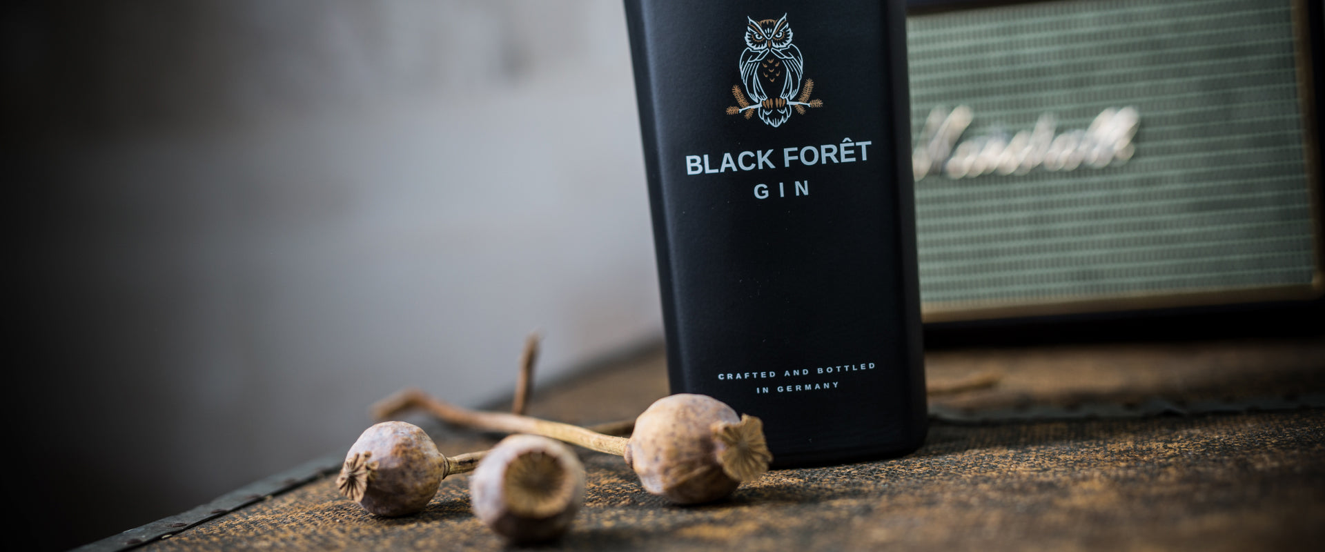 Schwarze Flasche Black Forêt Gin und Mohnkapseln auf rustikalem Tisch, neben einem Vintage-Radio.