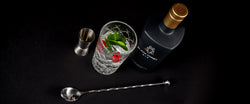 Flasche Gin, Glas mit Minze und Himbeeren, Messbecher und Barlöffel auf schwarzem Hintergrund.