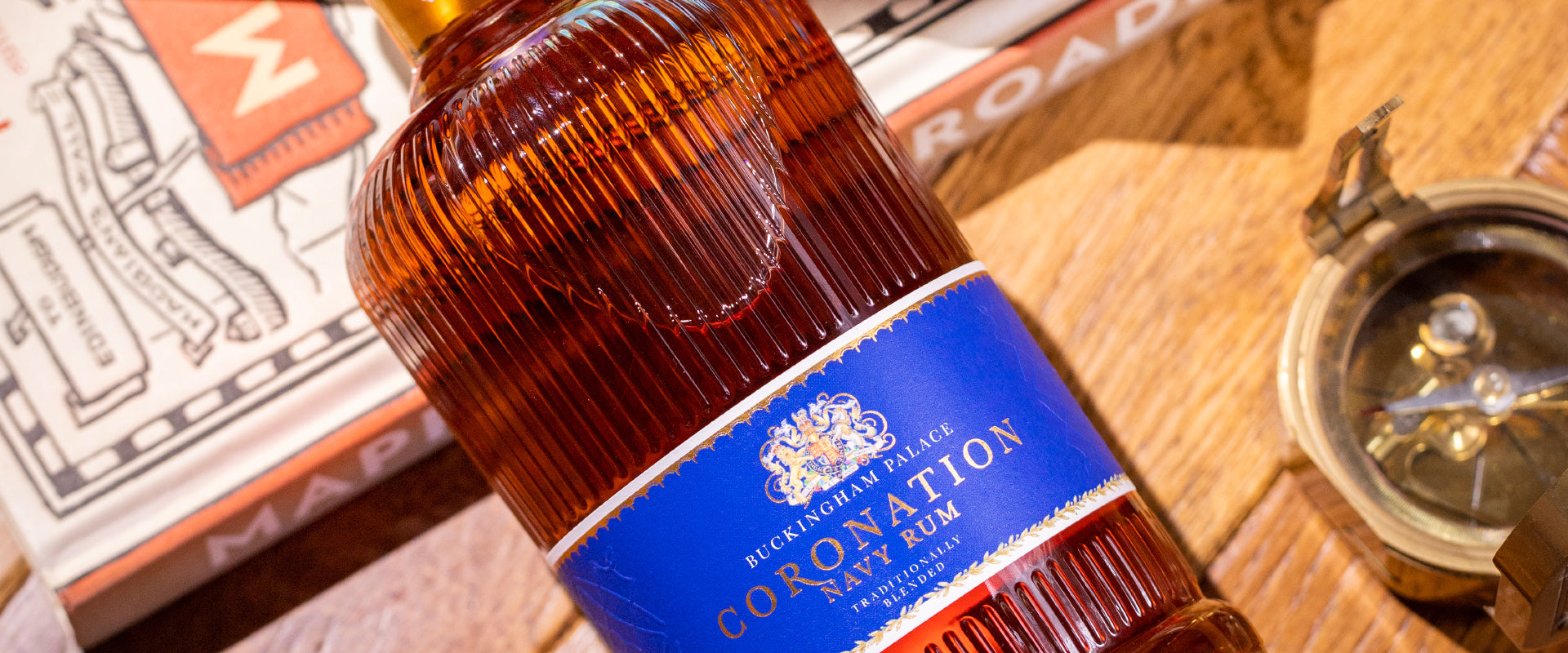 Eine Flasche Buckingham Palace Coronation Navy Rum liegt auf einem Holztisch neben einem Kompass und Karten.