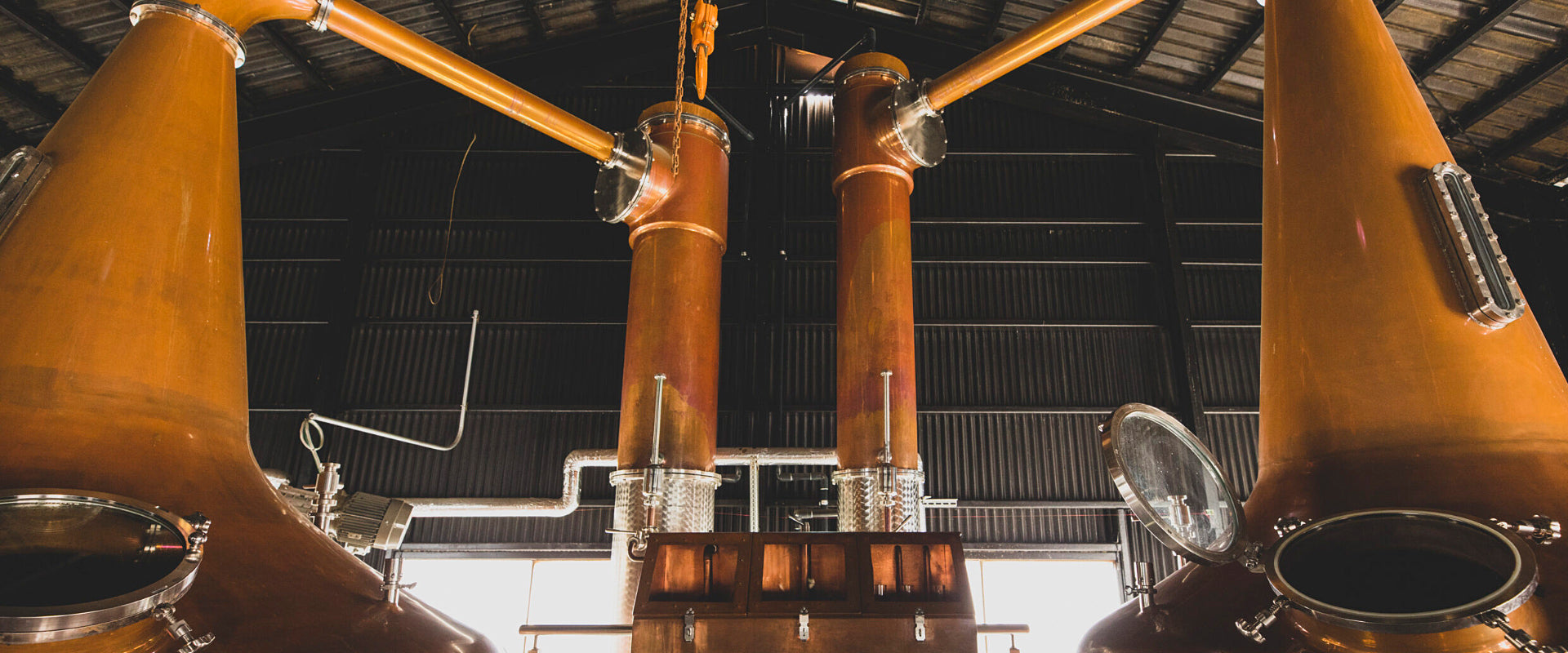 Innenansicht einer Brennerei mit großen kupfernen Brennblasen und Rohrleitungen.