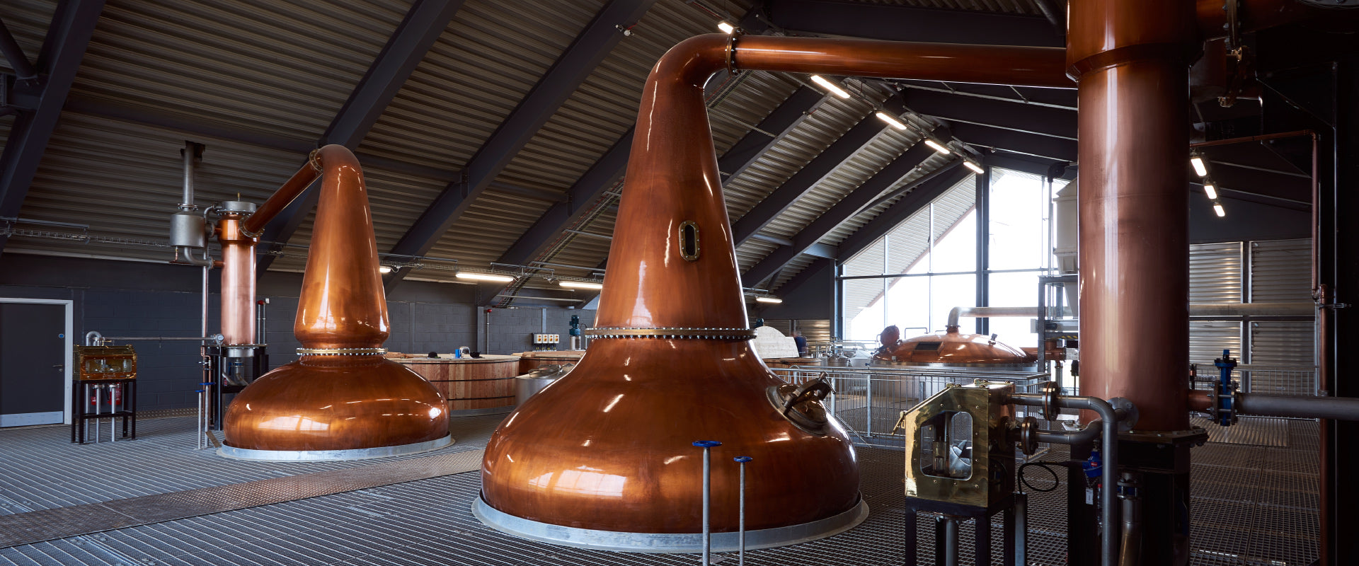 Kupferne Brennblasen in einer Destillerie mit industrieller Umgebung und moderner Architektur.