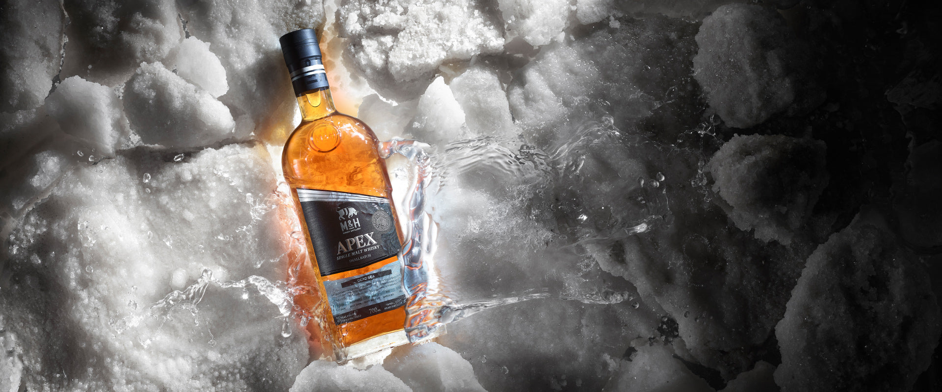 Eine Whiskyflasche liegt eingebettet in Eis und spritzendem Wasser.