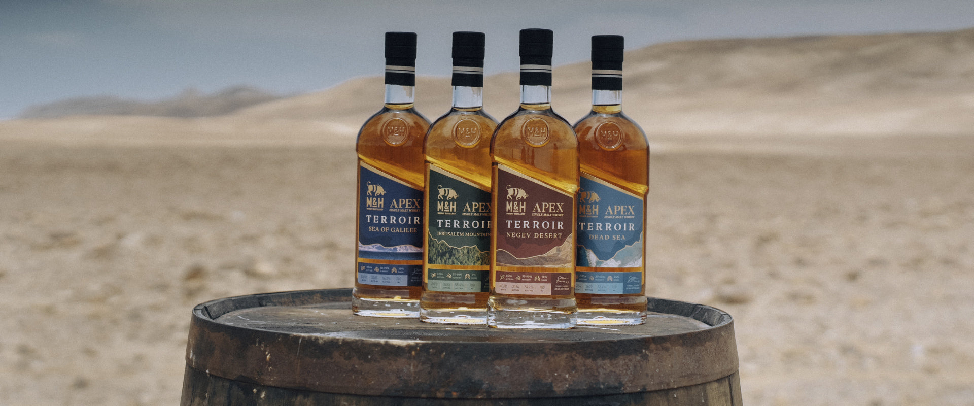 Vier Whiskyflaschen auf einem Fass vor einer Wüstenlandschaft.
