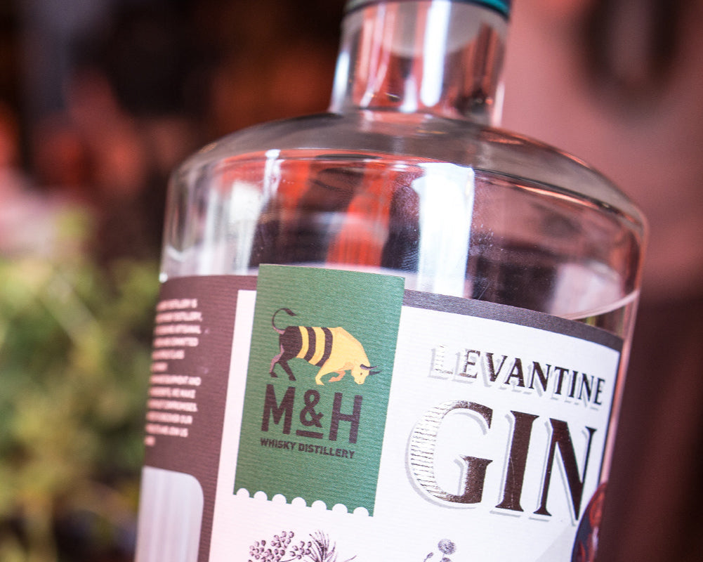Eine Flasche Levantine Gin von M&H Whisky Distillery mit Kräutern im Hintergrund.