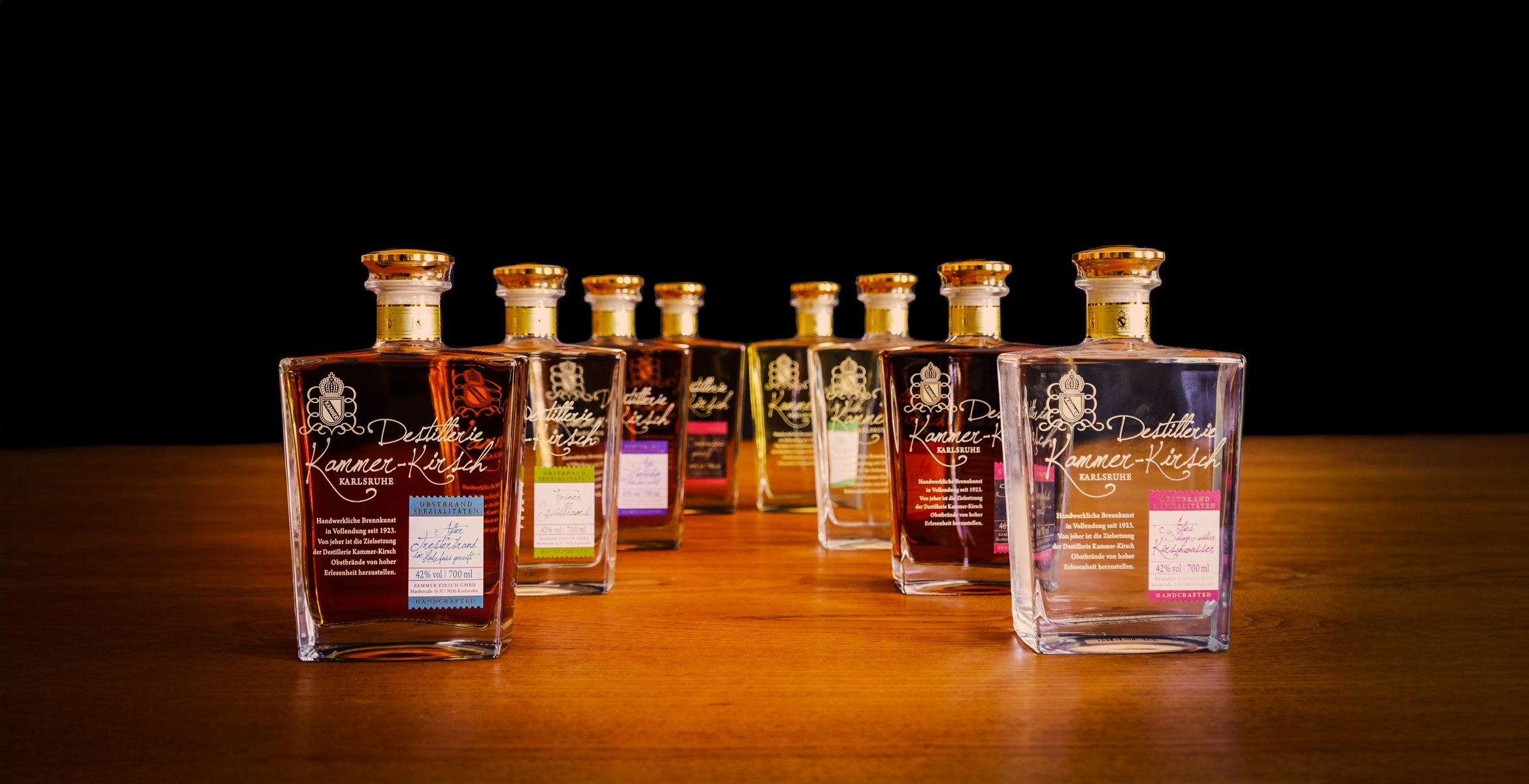 Eine Auswahl von Schnapsflaschen der Destillerie Kammer-Kirsch, auf einem Holztisch vor einem schwarzen Hintergrund.