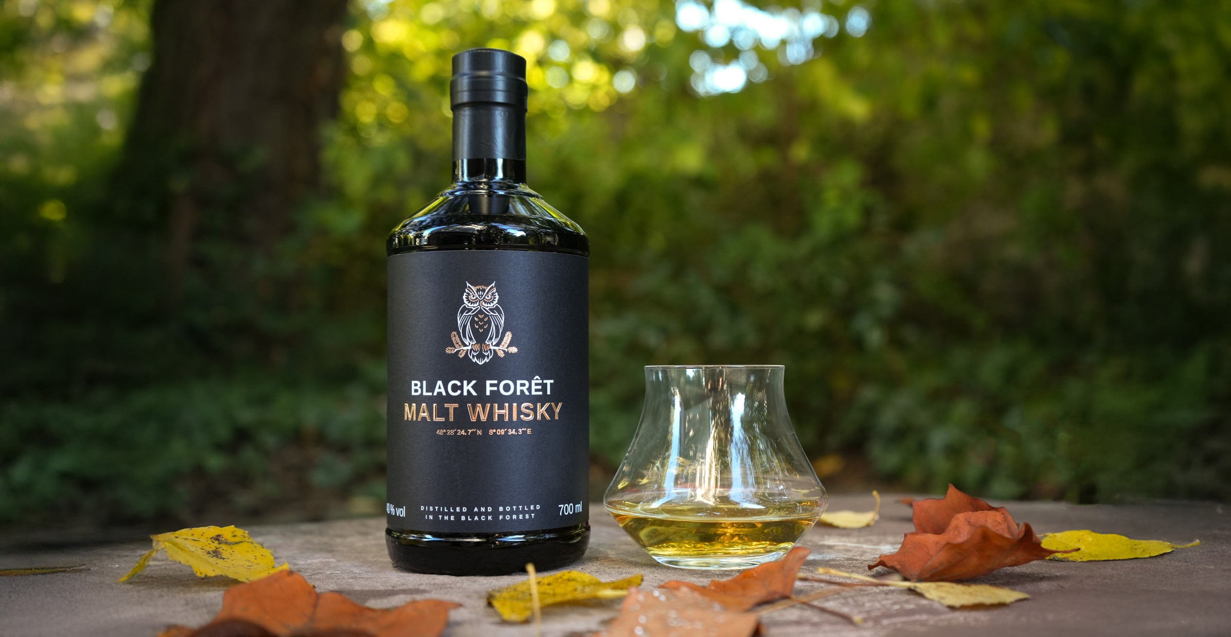 Whiskyflasche und Glas im Freien umgeben von Herbstlaub.