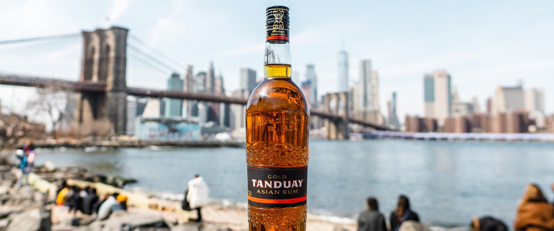 Eine Flasche Tanduay Rum mit dem verschwommenen Brooklyn Bridge und Manhattan im Hintergrund.