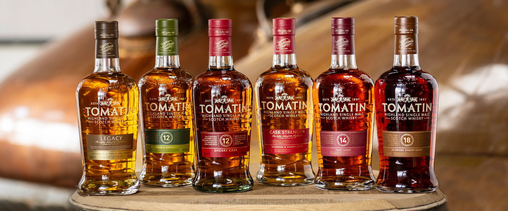 Sechs Flaschen Tomatin Highland Single Malt Whisky auf einem Holzfass.