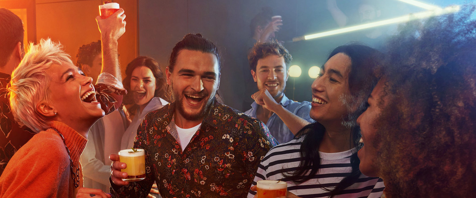 Menschen feiern zusammen fröhlich auf einer Party mit Getränken in den Händen und lachen.