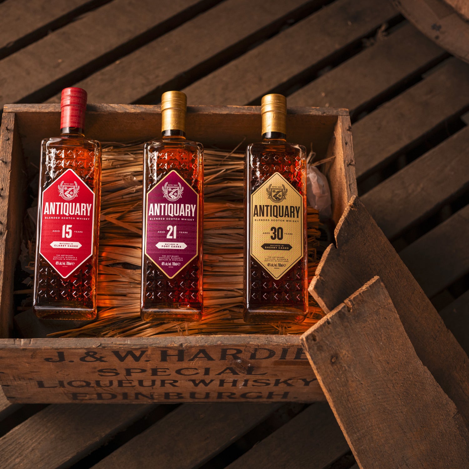 Drei Antiquary Whiskyflaschen im Holzrahmen auf einer Holzkiste präsentiert.