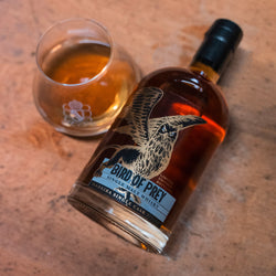 Flasche Bird of Prey Single Malt Whisky und ein Glas Whisky auf einem Holztisch.
