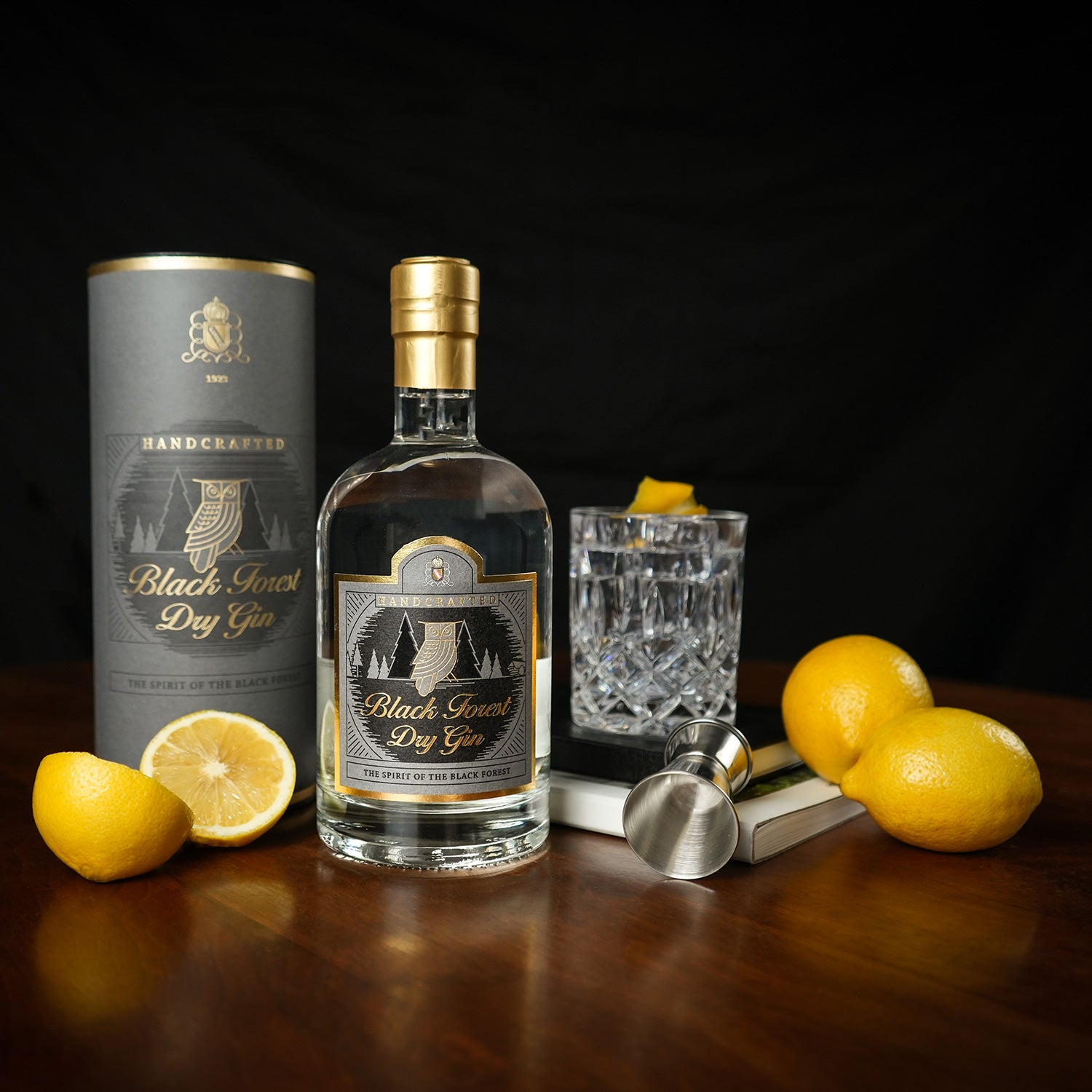 Eine Flasche Black Forest Dry Gin neben einem Glas, Zitronen und einem Jigger auf einem Holztisch.