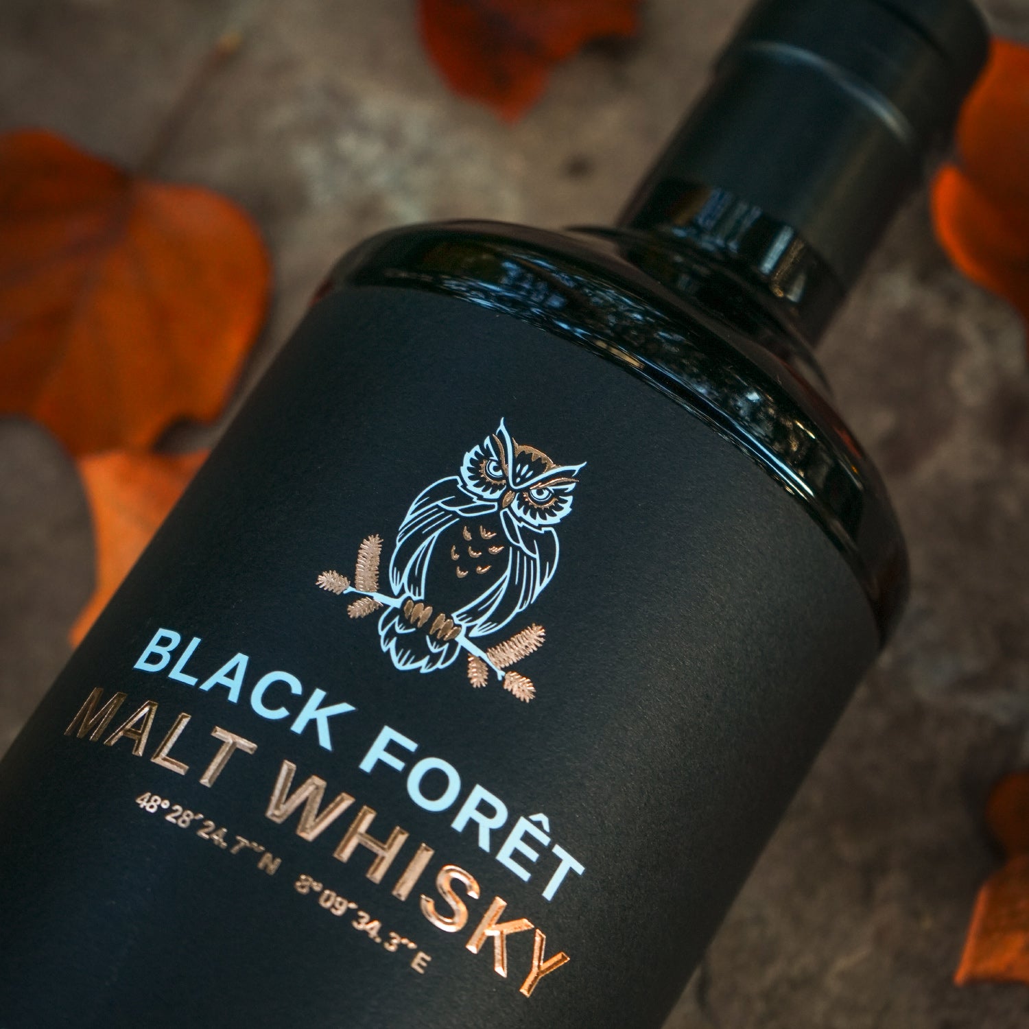 Eine Flasche Black Forêt Malt Whisky mit Eulenlogo auf herbstlichem Hintergrund.