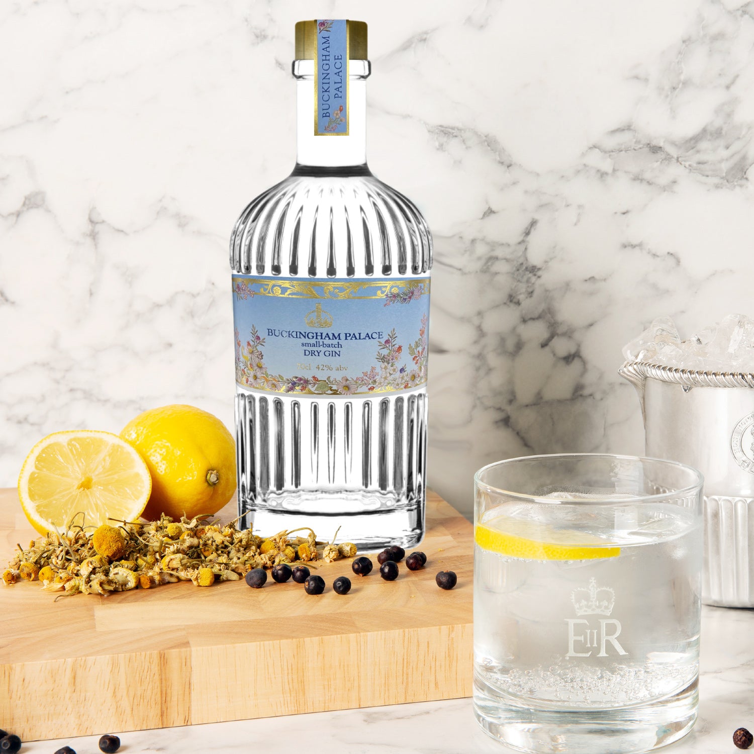 Buckingham Palace Dry Gin-Flasche mit Zitrone, Kamille und Wacholderbeeren auf Holzbrett, daneben ein Glas mit Gin Tonic.