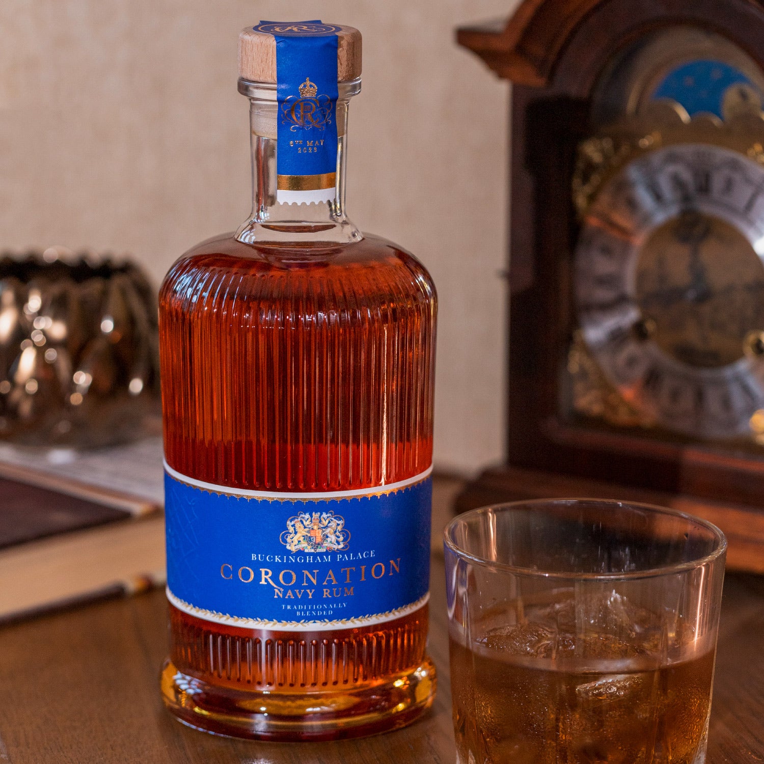 Eine Flasche Coronation Navy Rum neben einem gefüllten Glas und einer alten Uhr im Hintergrund.