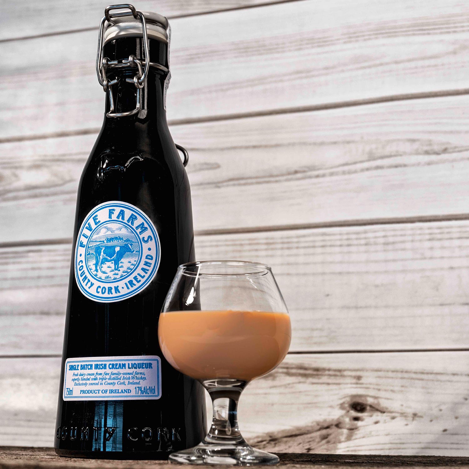 Eine Flasche Five Farms Irish Cream Likör und ein gefülltes Likörglas stehen auf einem Holztisch vor einer Holzwand.