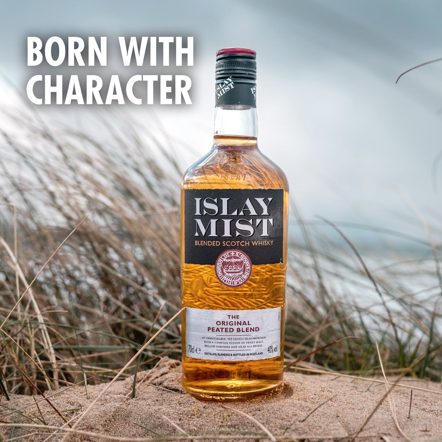 Eine Flasche Islay Mist Whisky steht in einer sandigen Dünenlandschaft, daneben der Text "Born with Character".