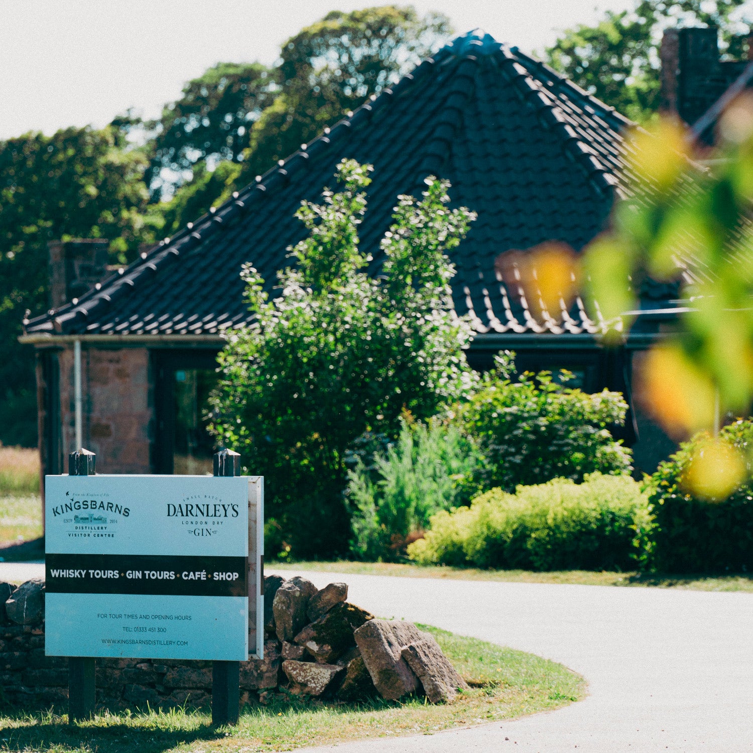 Ein Schild für eine Destillerie mit Whisky- und Gin-Touren vor einem Gebäude mit einem dunklen Ziegeldach.