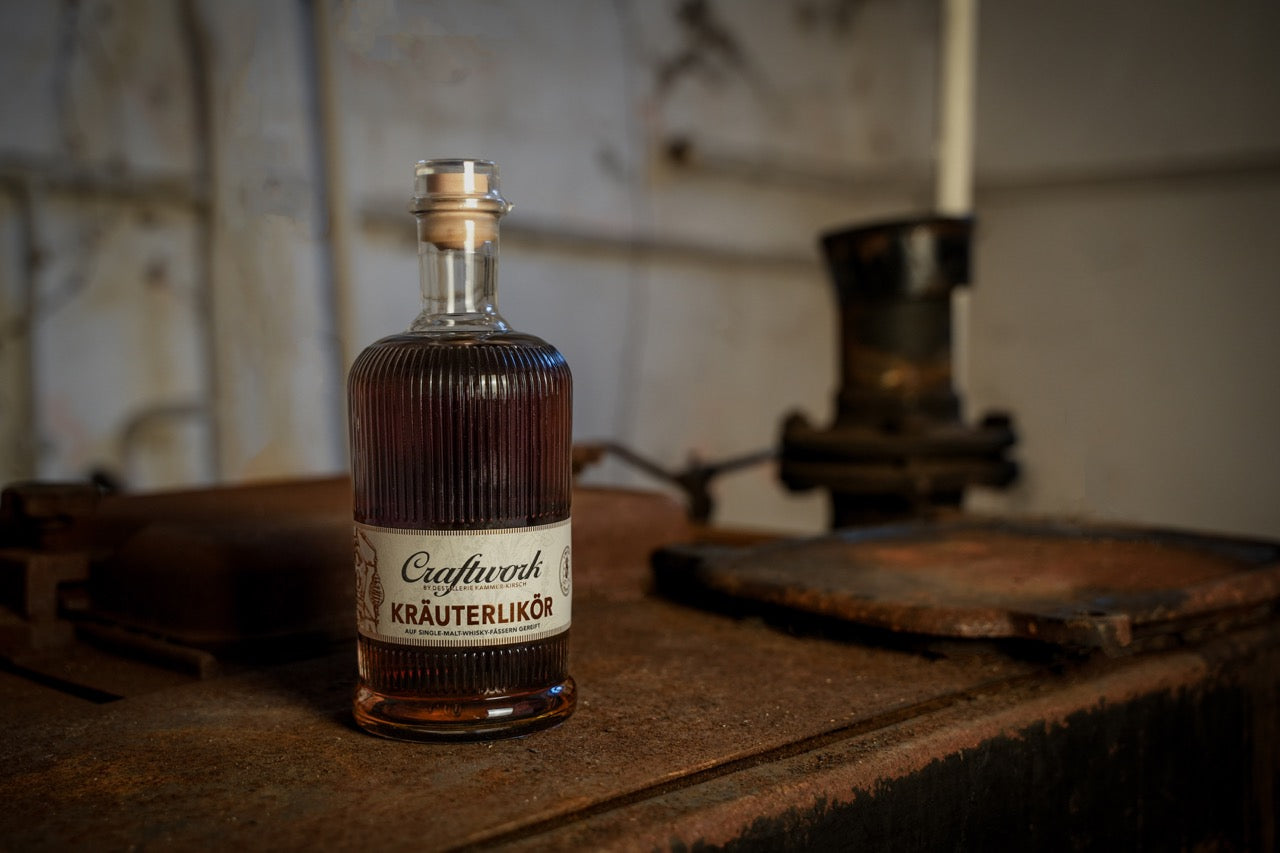 Eine Flasche Kräuterlikör steht auf einem rostigen, alten Tisch in einer industriellen Umgebung.