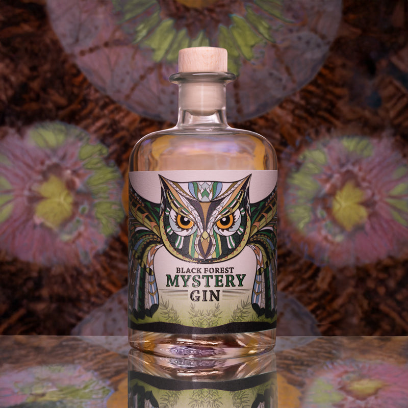 Flasche Black Forest Mystery Gin mit Eulenmotiv auf dem Etikett vor verschwommenem Hintergrund.
