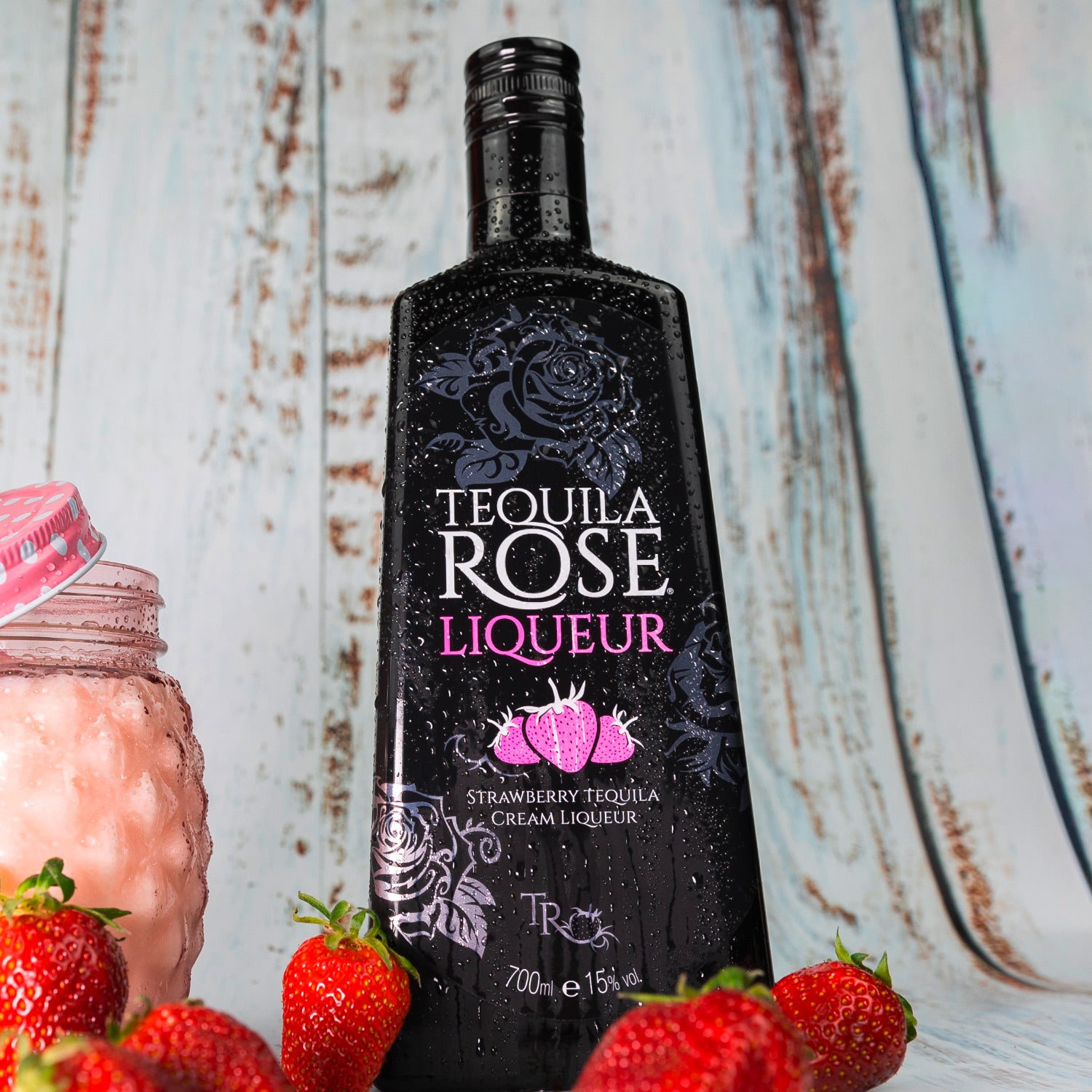 Eine schwarze Flasche Tequila Rose vor einem rustikalen Hintergrund, umgeben von frischen Erdbeeren.