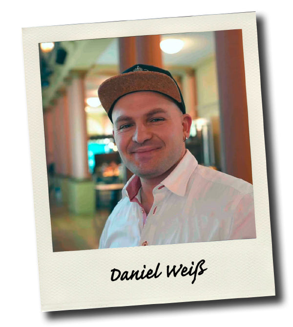 Mann mit Baseballkappe lächelt in die Kamera, im Hintergrund eine helle Inneneinrichtung.