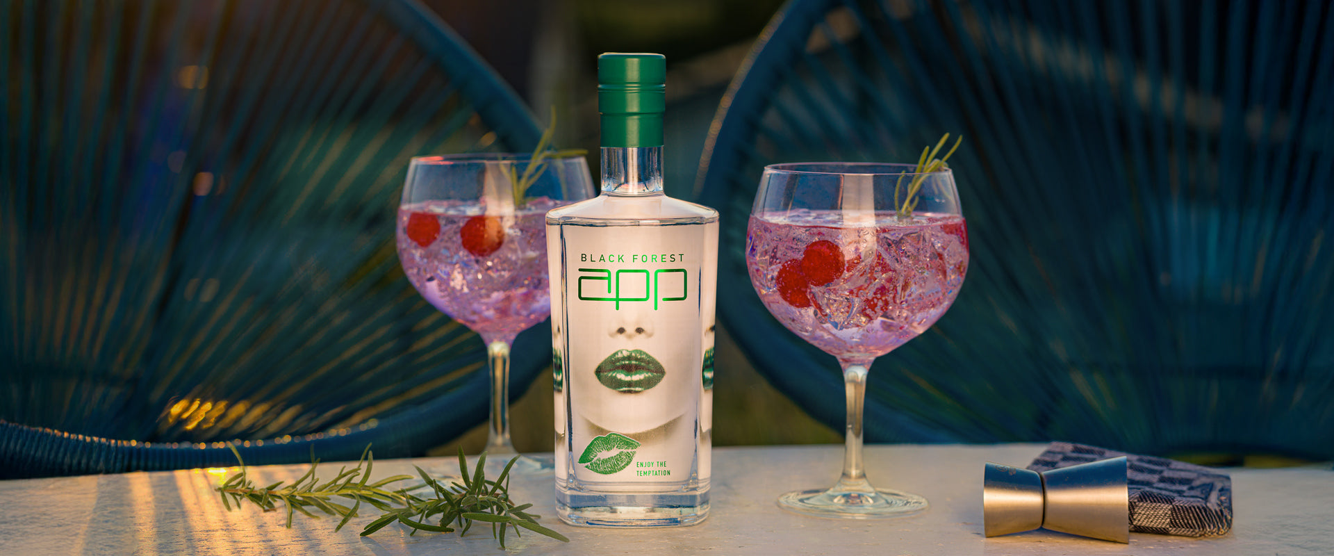 Eine Flasche Black Forest Gin mit zwei Cocktails auf einem Tisch, dekoriert mit Rosmarin und Himbeeren.
