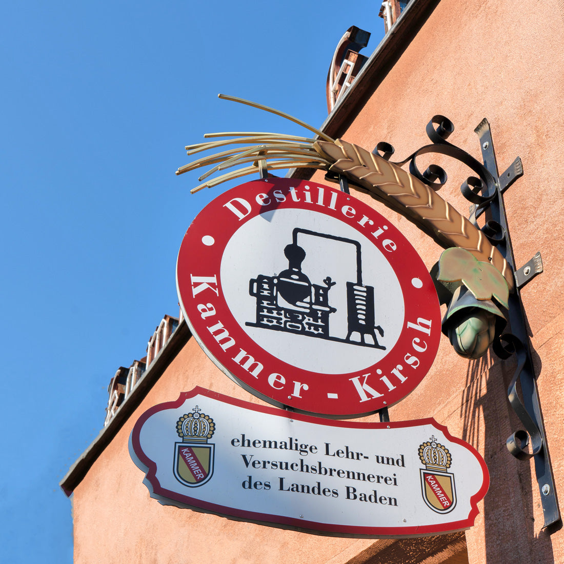 Ein Schild der Destillerie Kammer-Kirsch an einer Hauswand unter blauem Himmel.